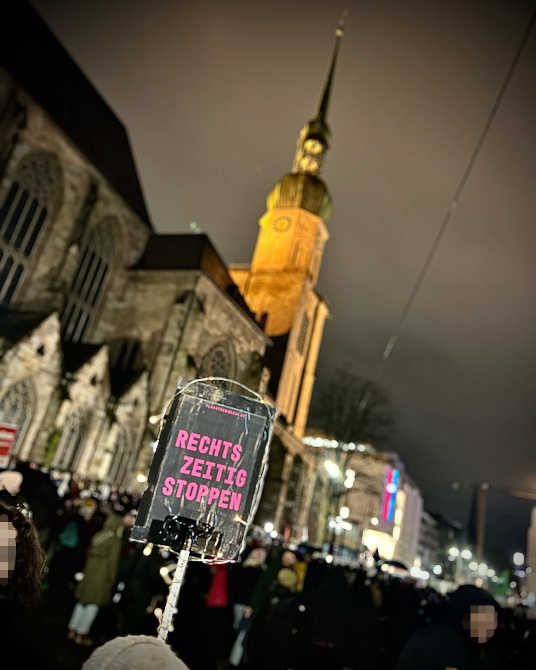 Eine große Menge Demonstranten vor der im Hintergrund zu sehenden Reinoldikirche in Dortmund bei Nacht. Im Vordergrund ein Schild an einer Tragestange mit der Aufschrift "Rechts zeitig stoppen"